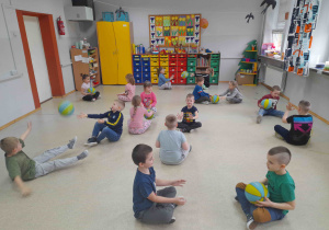 Dzieci w siadzie skrzyżnym rzucają do siebie piłki